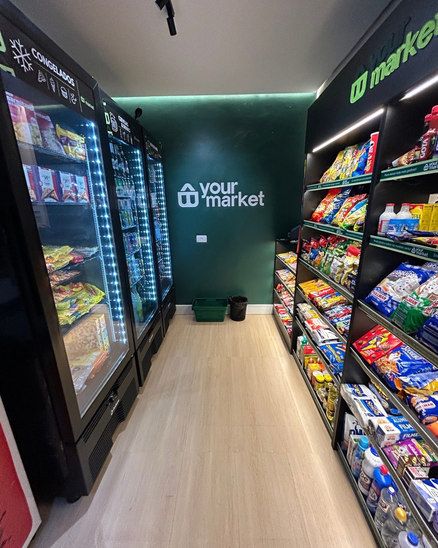 Loja Your Market em operação, com geladeiras e prateleiras abastecidas e o logo iluminado na parede verde